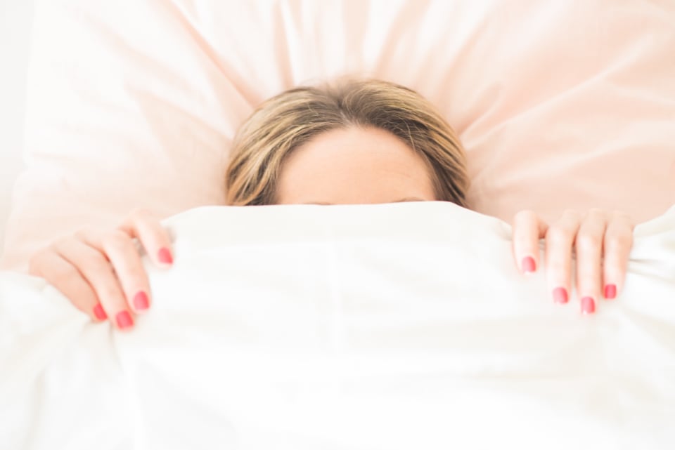 Woman peeking out from under a white duvet