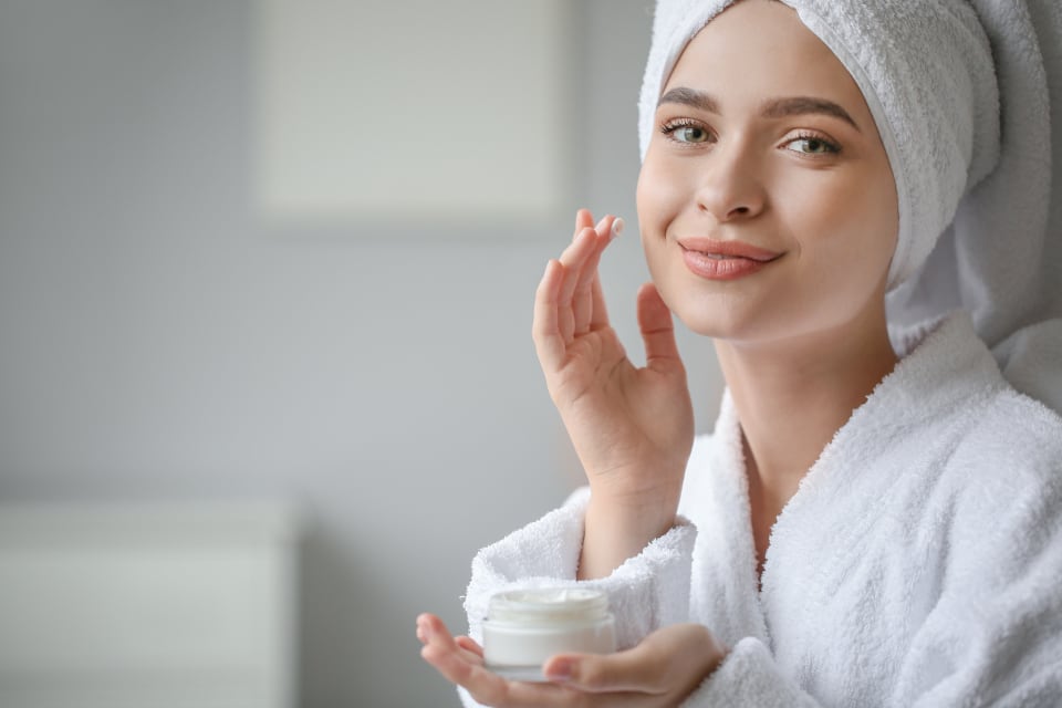 Woman in a bathrobe and towel applying face cream at home
