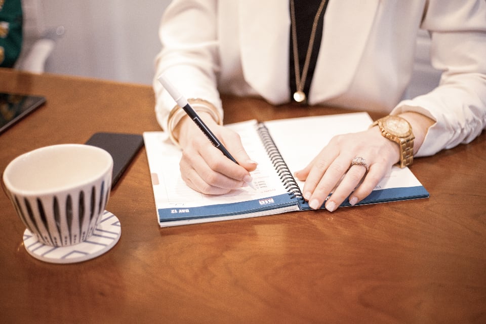 Woman writing in a planner next to a cup of coffee