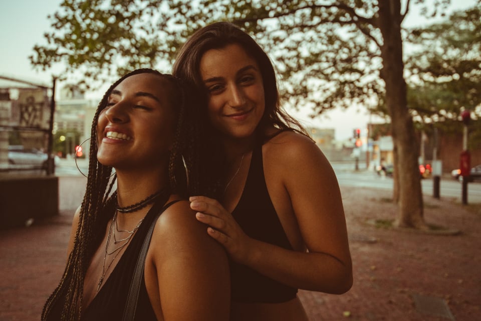 Two women friends smiling together outdoors at sunset